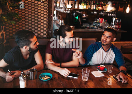 Gruppo di razza mista giovani uomini che parlano in un lounge bar. Multirazziale amici divertendosi in cafe di bere il caffè Foto Stock