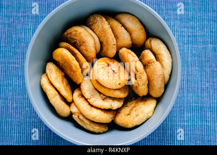 Vista superiore del blu ciotola riempita con il mucchio di dolci fichi secchi e composto sul tessuto blu Foto Stock