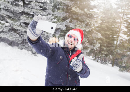 I giovani di moda uomo mostra Thumbs up tenendo autoritratto nella foresta. Scena d'inverno. Foto Stock