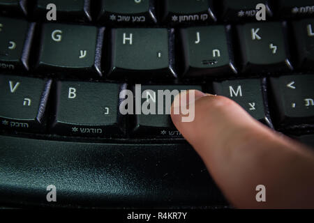 Man digitando su una tastiera con lettere in ebraico e in inglese Foto Stock