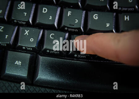 Man digitando su una tastiera con lettere in ebraico e in inglese Foto Stock