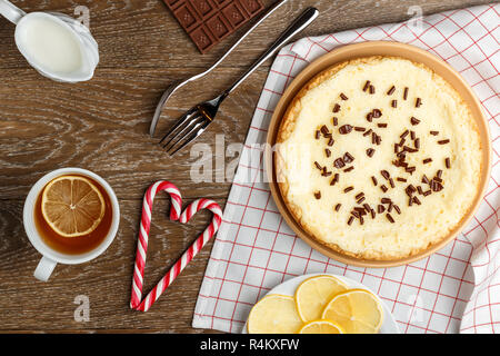 In casa la cheesecake cosparso con scaglie di cioccolato, tè con limone e caramella di Natale a forma di cuore su uno sfondo in legno.Vista Superiore Foto Stock