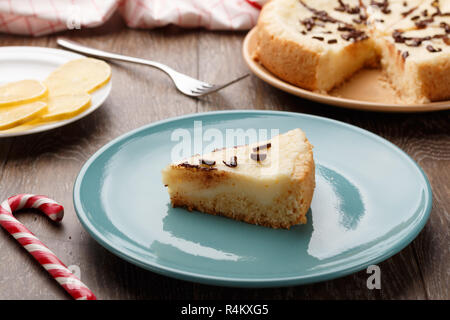 In casa la cheesecake cosparso con scaglie di cioccolato su una piastra di blu. Sfondo di legno, vista laterale Foto Stock