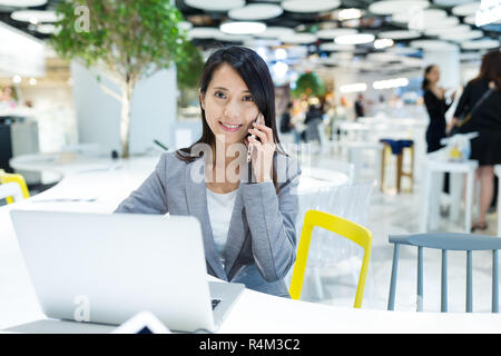 Imprenditrice parlare al telefono cellulare e utilizzando il computer portatile in share office Foto Stock