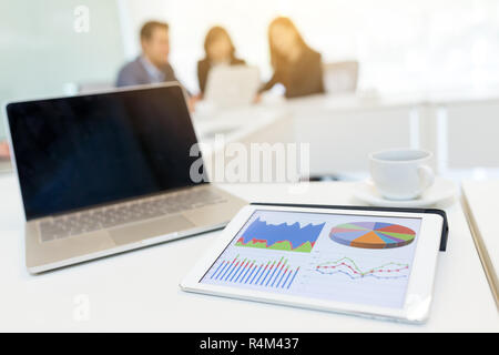 Tavoletta digitale che mostra i dati grafico su schermo e schermo vuoto del computer portatile a sala riunioni Foto Stock