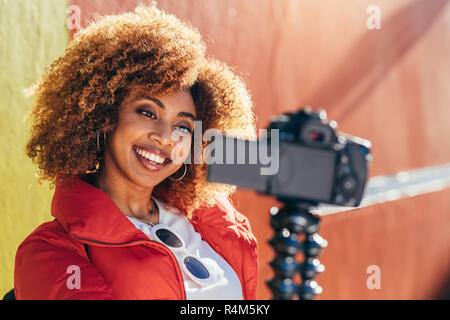 Allegro afro american donna contenuti della registrazione per il suo blog di viaggio all'esterno. Ritratto di una donna turistica prendendo un selfie all'aperto con una fotocamera reflex digitale. Foto Stock