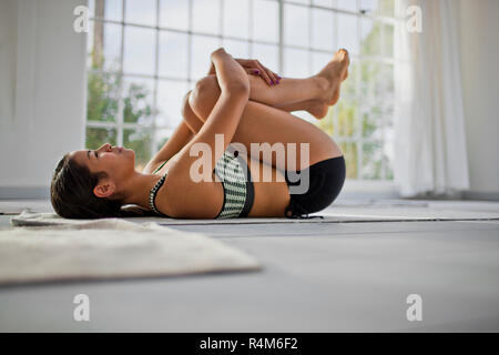 Giovane donna abbracciando le ginocchia al petto dopo una sessione di yoga. Foto Stock
