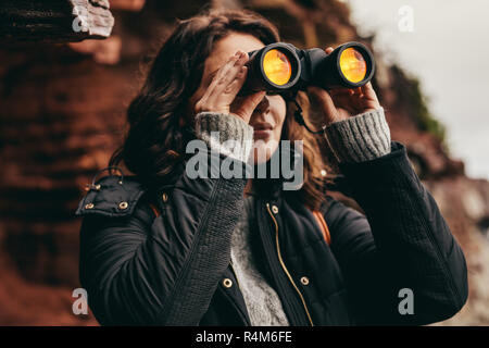 Giovane donna in natura e gode di vista utilizzando il binocolo. Donna cerca di viaggiatori attraverso il binocolo. Foto Stock