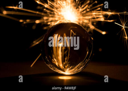 Burning sparkler dietro una palla di vetro su uno sfondo nero. Foto Stock