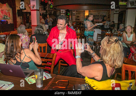 Indossa una tuta rossa, un medio orientale americana Elvis Presley impersonator intrattiene gli adulti e gli anziani ad una Santa Ana CA pub come essi fotografarlo con smart phone telecamere. Foto Stock