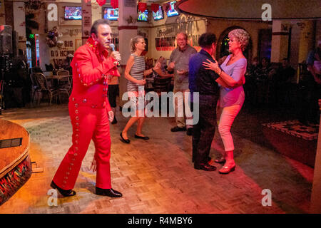 Indossa una tuta rossa, un medio orientale americana Elvis Presley impersonator intrattiene gli adulti e gli anziani ad una Santa Ana CA pub. Foto Stock