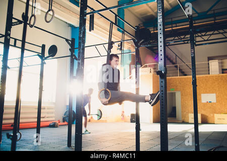 Muscolo-up esercizio athletic uomo facendo un intenso allenamento in palestra su anelli di ginnastica. Foto Stock