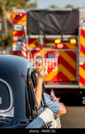 Una bandiera americana sventola dalla finestra di un antico 1951 auto della polizia in quanto segue un incendio del motore in un quarto di luglio sfilata in Newport Beach, CA. Foto Stock