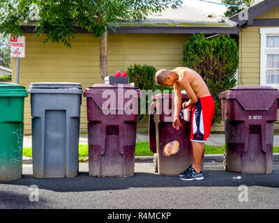 Un determinato senzatetto uomo ispanico cerca street cestino contenitori per cibo e gli oggetti di valore in Santa Ana CA. Foto Stock