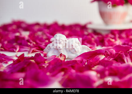 Statuetta di due antichi piccoli angeli incantevole del gesso su sfondo bianco con rosa peonia viola petali di fiori. Amore, romantico, Valentines d Foto Stock