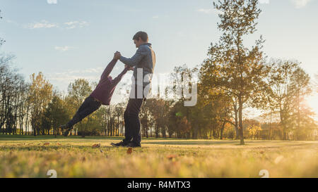 Padre la filatura suo figlio toddler tenendo lui dalle sue mani al di fuori in autunno park. Foto Stock