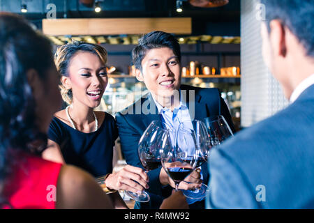 Amici asiatici tostare con vino rosso in bar Foto Stock