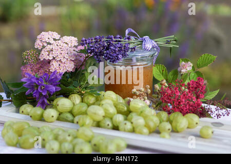 Atmosfera estiva con uva spina sul vassoio in legno amorevolmente decorate con fiori e vasetto di marmellata Foto Stock