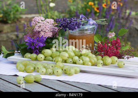 Atmosfera estiva con uva spina sul vassoio in legno amorevolmente decorate con fiori e vasetto di marmellata Foto Stock