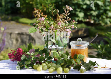 Atmosfera estiva con uva spina sul vassoio in legno amorevolmente decorate con fiori e vasetto di marmellata Foto Stock