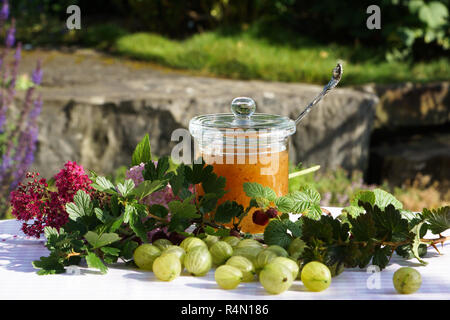 Atmosfera estiva con uva spina sul vassoio in legno amorevolmente decorate con fiori e vasetto di marmellata Foto Stock