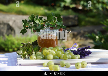 Atmosfera estiva con uva spina sul vassoio in legno amorevolmente decorate con fiori e vasetto di marmellata Foto Stock