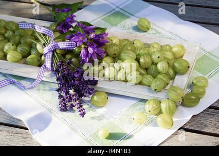 Atmosfera estiva con uva spina sul vassoio in legno amorevolmente decorate con fiori e vasetto di marmellata Foto Stock