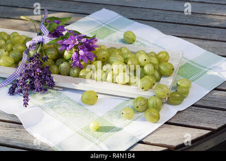 Atmosfera estiva con uva spina sul vassoio in legno amorevolmente decorate con fiori e vasetto di marmellata Foto Stock