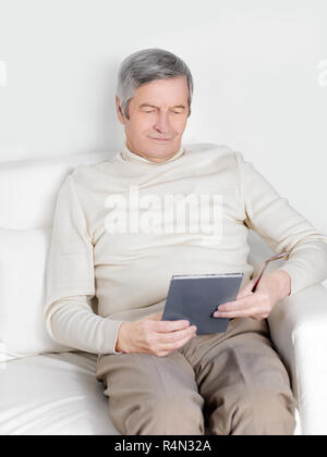 Bello il vecchio uomo in abbigliamento casual è utilizzando una tavoletta digitale Foto Stock