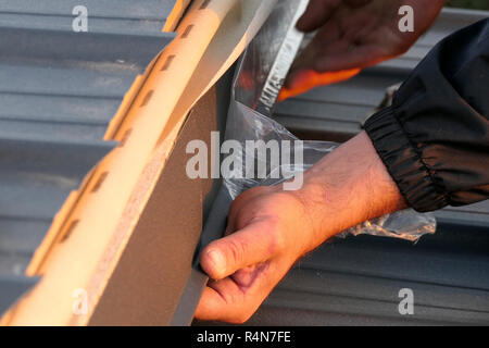 Uomo al lavoro su tetto lamiera nella costruzione del sito. Elementi di finitura. Foto Stock