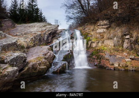 Splendida Mountain Creek Waterfall a cascata verso il basso la parete rocciosa e colori d'autunno foglie rosse Foto Stock