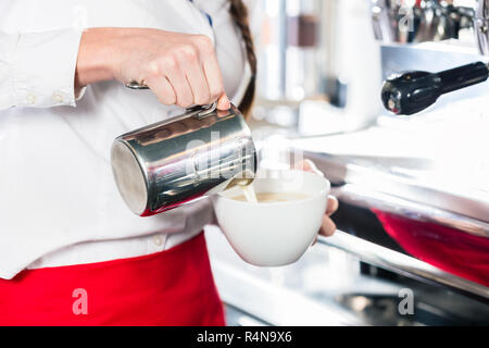 Close-up di mani di una cameriera versando il latte in una tazza di caffè Foto Stock