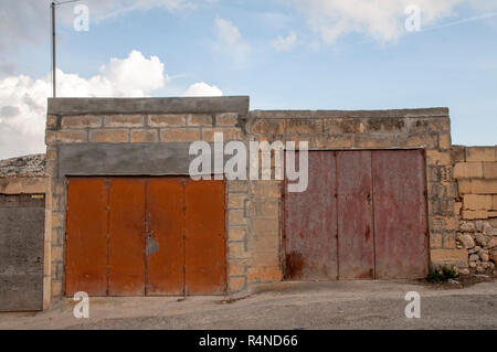 Garage a Gozo, Malta, con rusty in metallo colorato porte impostato in una brezza blocco parete anteriore. Foto Stock