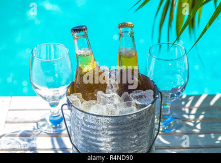 Vista ravvicinata del secchiello per il ghiaccio con la birra su di un tavolo di legno accanto alla piscina. Foto Stock