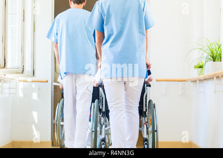 Gli infermieri spingendo gli anziani in carrozzella thru nursing home Foto Stock