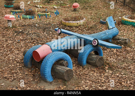 Aeroplano giocattolo realizzato da rifiuti pneumatici e tronchi di legno sul bambino giochi per bambini in Ivanovo, Russia. Letti di fiori realizzato da rifiuti pneumatici e funghi rossi ricavati da antichi lavabi e tronchi di legno sono visti in background. Attenzione: Questa immagine è una parte di un saggio fotografico di 18 foto con lo stesso campo giochi. Foto Stock