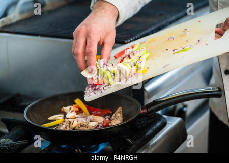 Chef di mettere gli ingredienti in padella ristorante cucina Foto Stock