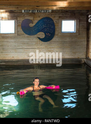 Solo metà donna adulta nuoto nella piscina termale calda all'interno di un fienile, Estate Lago, Oregon, Stati Uniti d'America Foto Stock