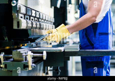 Due operai industriali ispezione pezzo da lavorare in piedi sul pavimento di fabbrica con cuffie e occhiali protettivi Foto Stock