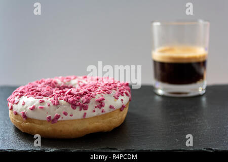 Ciambella con glassa bianca e rosa spruzza e una tazza di caffè nero Foto Stock
