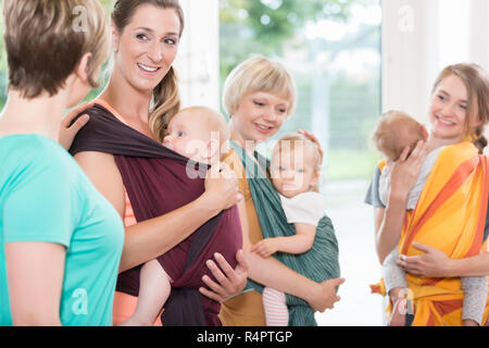 Il gruppo di donne a imparare a utilizzare imbracature bambino per madre-bambino l'incollaggio Foto Stock