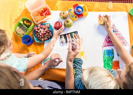 Scolare e scolari pittura durante la pausa pranzo con frutti e sandwich Foto Stock
