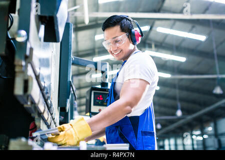 Due operai industriali ispezione pezzo da lavorare in piedi sul pavimento di fabbrica con cuffie e occhiali protettivi Foto Stock