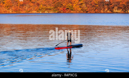 Un uomo anziano passeggiate in mare calmo su un gonfiabile sup board contro lo sfondo della Far Eastern Shore D'AUTUNNO Foto Stock