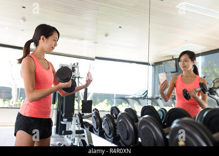 Le pratiche di donna sollevamento pesi e tsking selfie in palestra Foto Stock