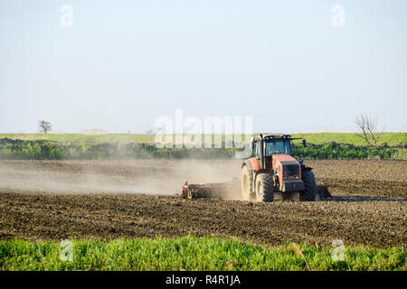 Un trattore con un aratro stabilisce il terreno. La coltivazione del suolo sul fie Foto Stock