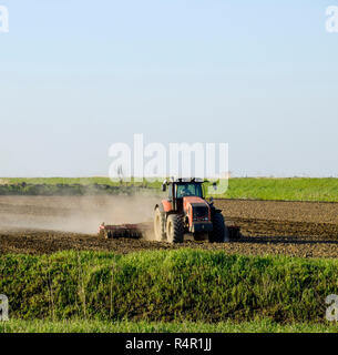 Un trattore con un aratro stabilisce il terreno. La coltivazione del suolo sul fie Foto Stock