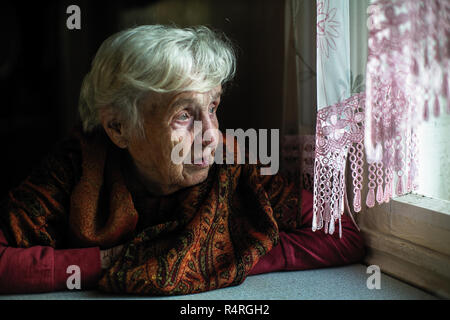 Donna anziana longingly guarda fuori dalla finestra. Foto Stock