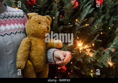 Scena di natale - donna azienda orsacchiotto e sparkler prima dell albero di natale Foto Stock