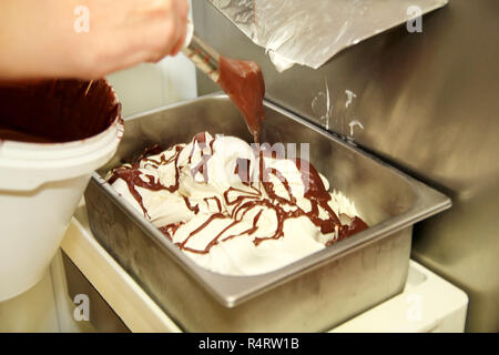 La donna lavora al gelato è in fabbrica decorazioni di cremoso gelato alla vaniglia con cioccolato medicazione in contenitore in acciaio. Colata di cioccolato. Foto Stock